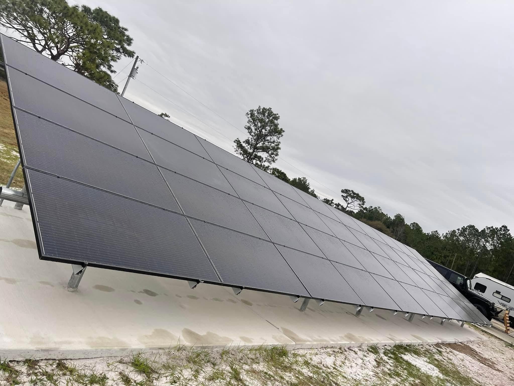 Large array of ground-mounted solar panels on a concrete pad under an overcast sky.