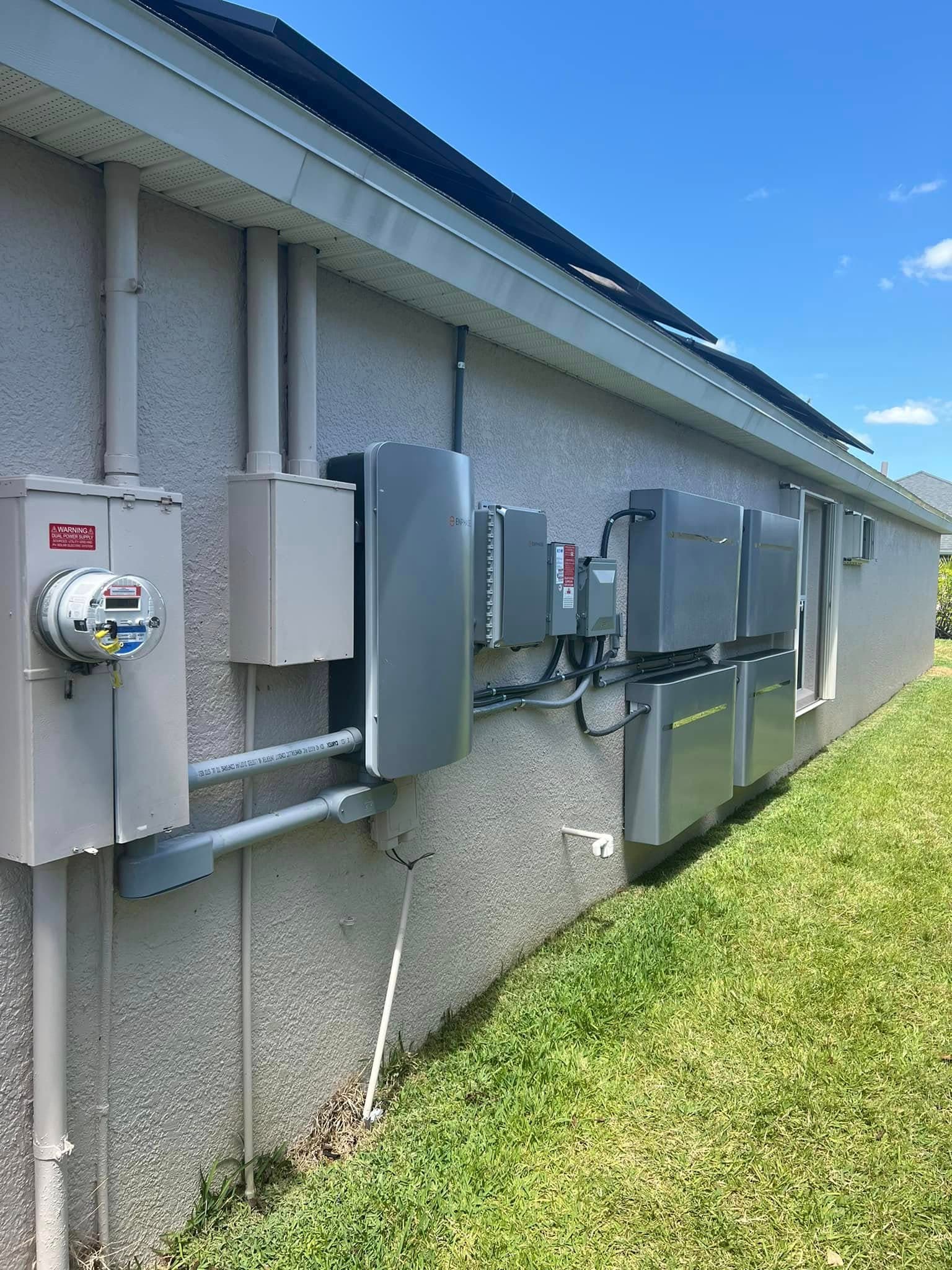 Solar energy system with battery storage units and electrical meters on a residential exterior wall.