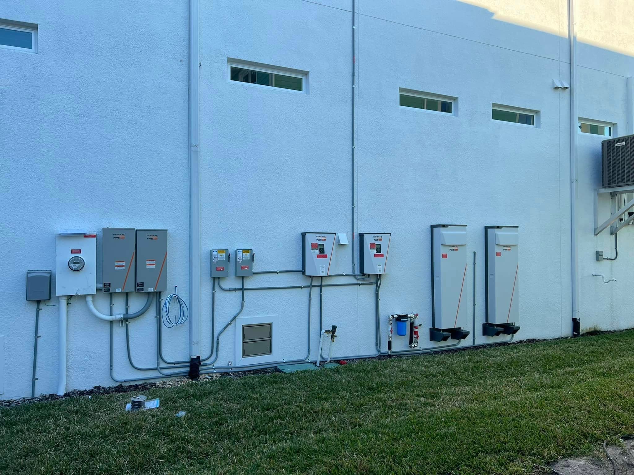 Generac solar battery storage units and electrical inverters mounted on a white exterior wall.