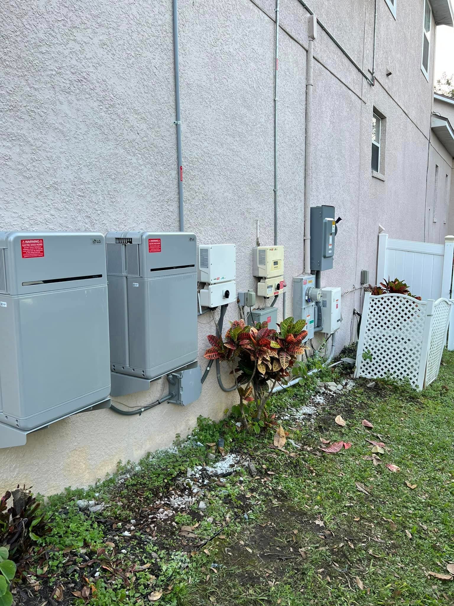 Two LG solar battery storage units and electrical equipment mounted on a residential stucco wall.