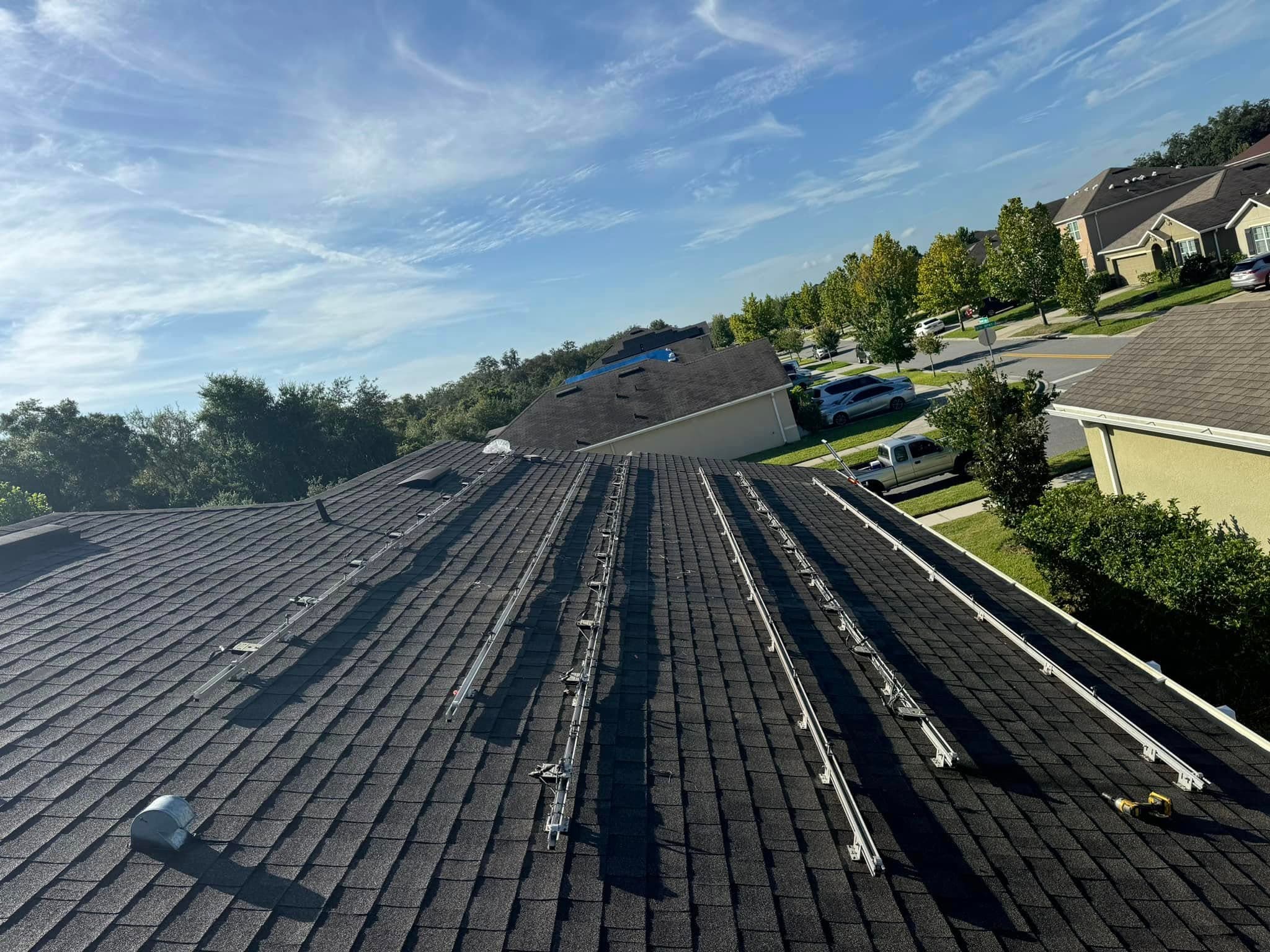 Solar panel mounting rails installed on a dark shingled residential roof under a blue sky.