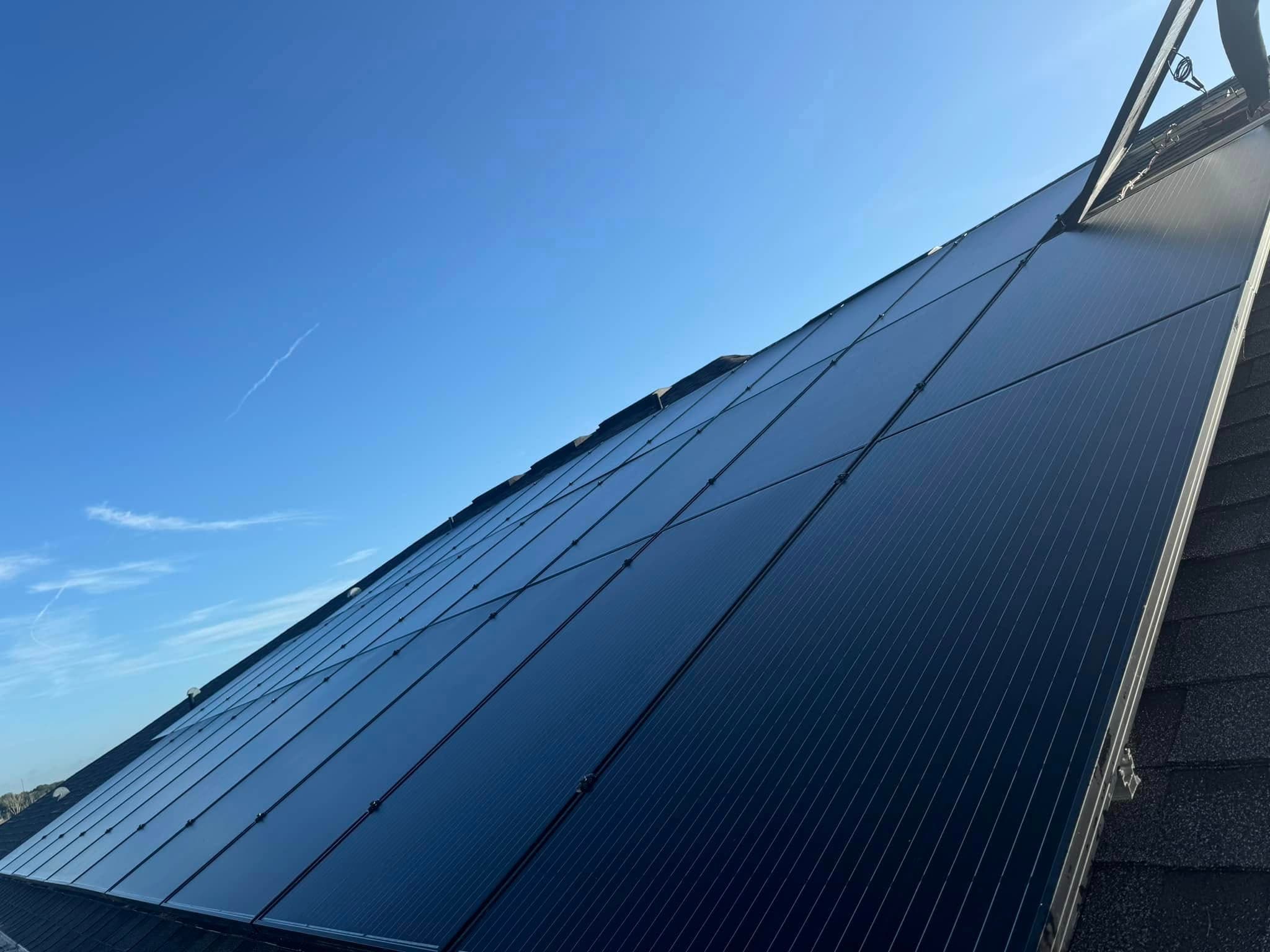 Modern black solar panels covering a slanted roof against a bright, clear blue sky.